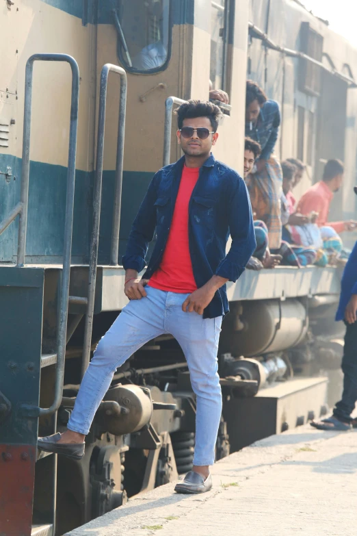 a man standing next to train on the tracks with a crowd of people walking