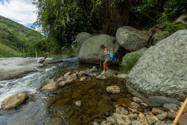 woman with backpack hiking down stream by boulders