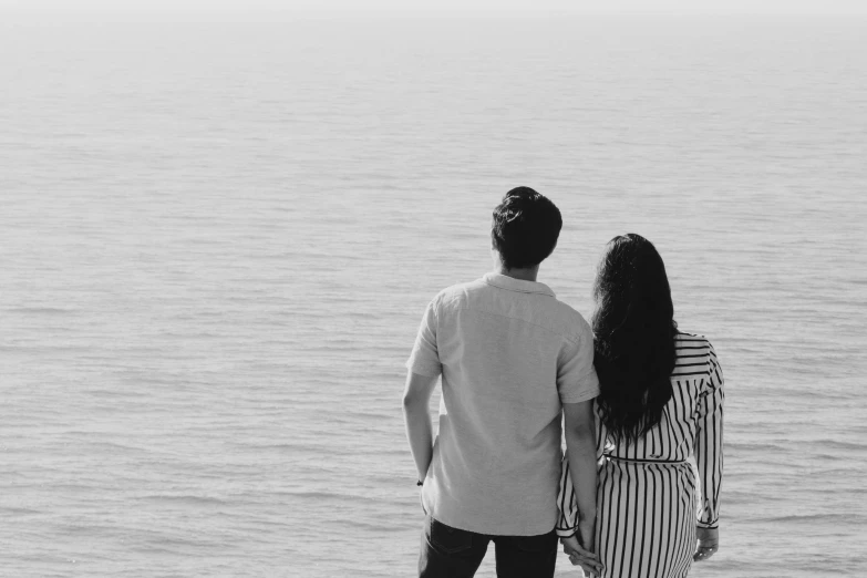 man and woman standing back to back on a beach looking out at the ocean