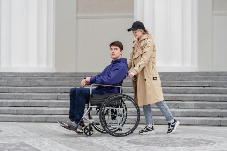 a woman in a trench coat sitting in a wheelchair being hed on stairs