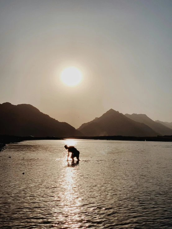 a person standing in the water near mountains