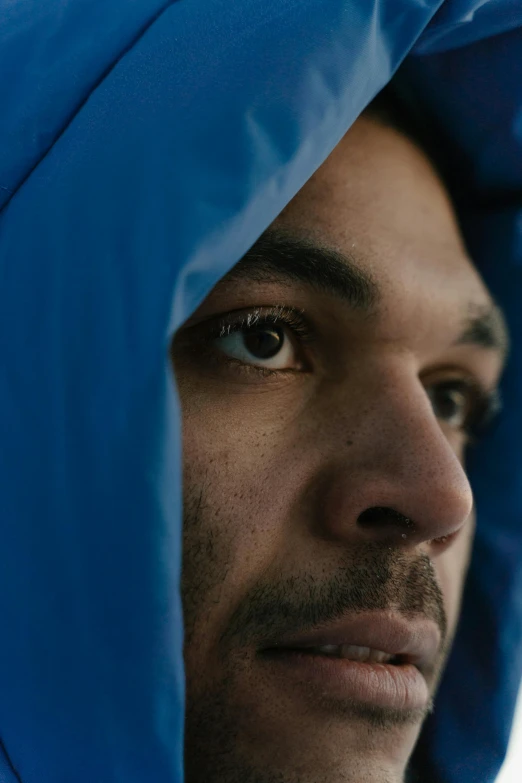 a close up image of the head and shoulders of a man with an unoned blue cloak on his head