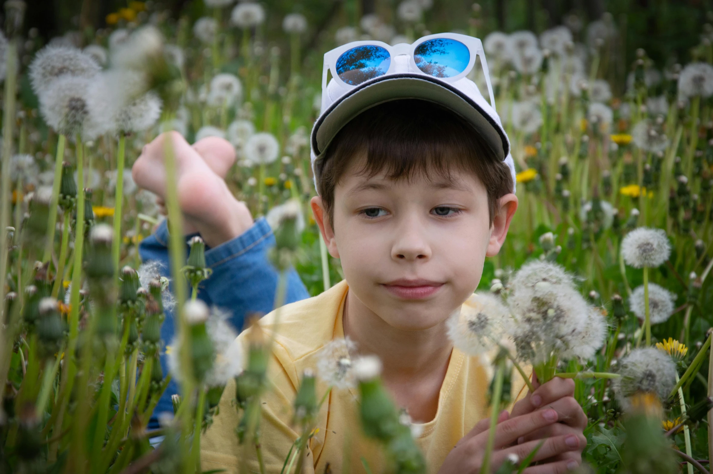 boy laying in grass with two hats on his head