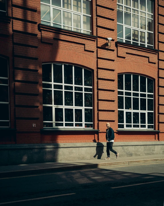 a man in a black coat walks near an orange brick building