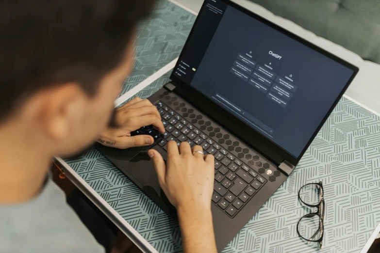 man typing on laptop with eyeglasses on table