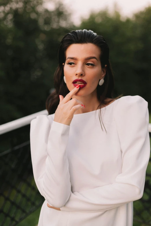 a woman is posing in the park, with her finger in her mouth