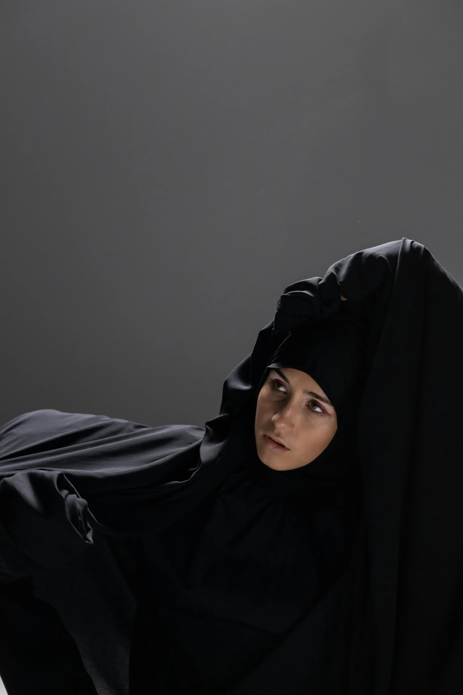 a woman in a black hijab looks up as she poses on her belly