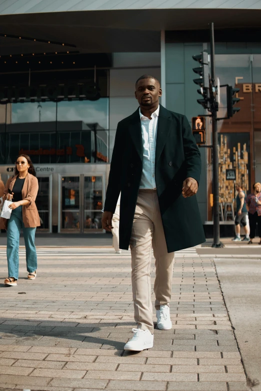 a man in a coat and shirt walking down a sidewalk