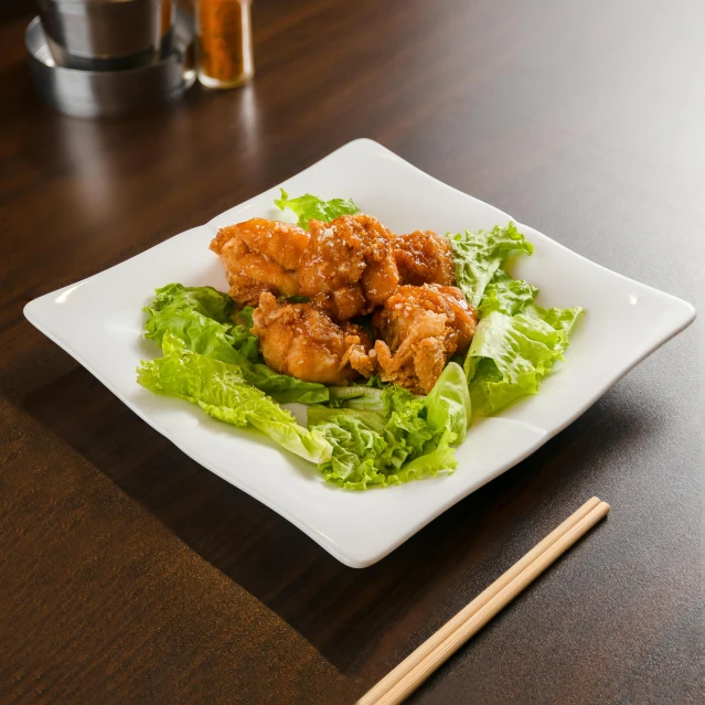 a square plate topped with chicken and lettuce next to chop sticks