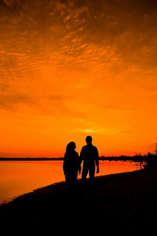 two people holding hands as the sun sets over water