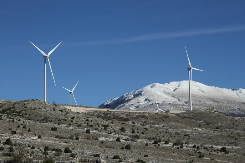 four wind turbines and two snow capped mountains in the background