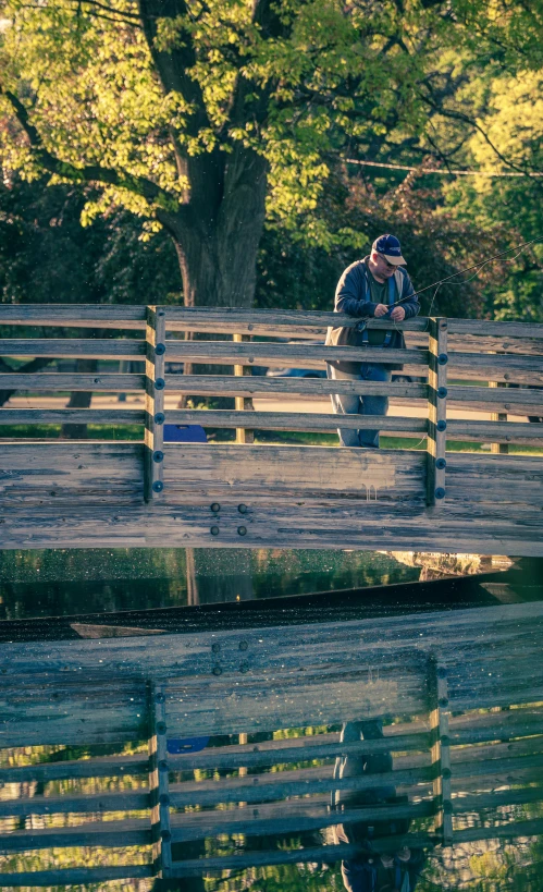 a man sits on a wood and metal bridge with water below