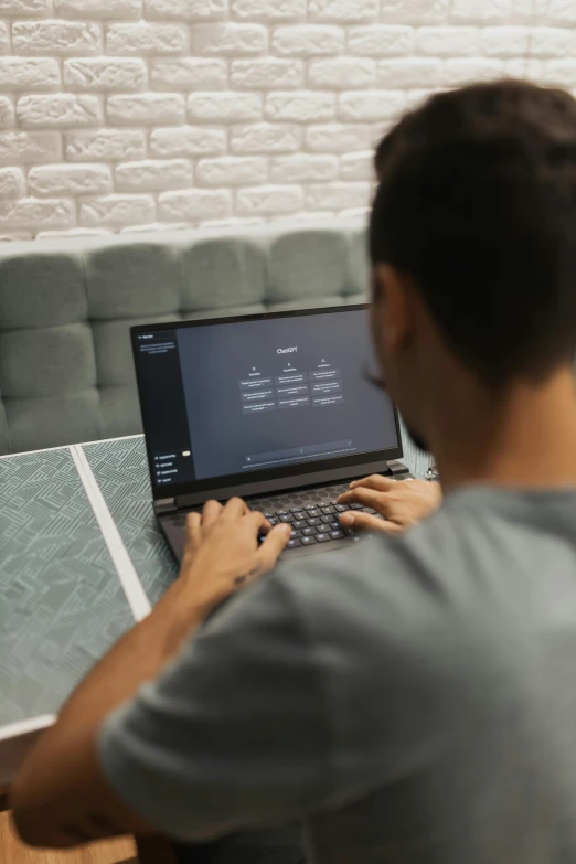 the man sits at a table while using his laptop