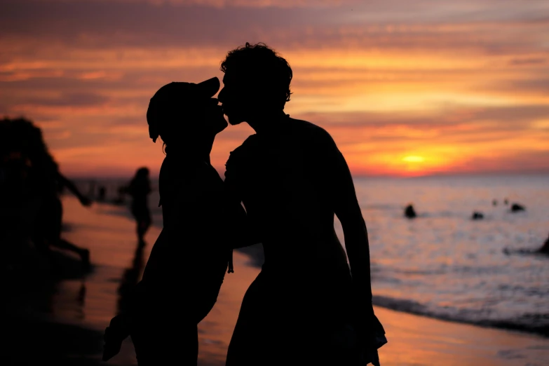 two people are standing near water as the sun sets