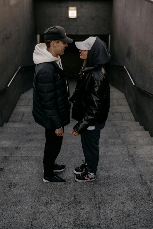 a man standing next to a woman in a black jacket and hood