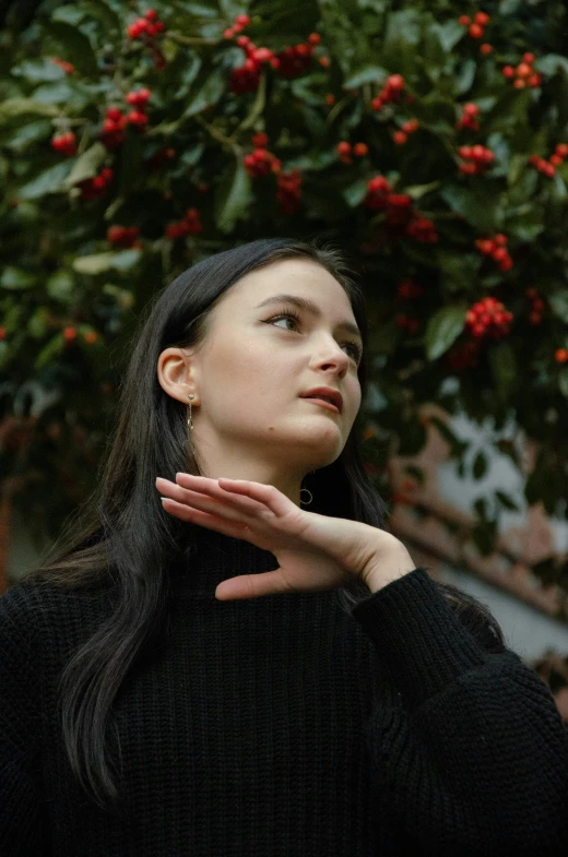 a woman standing in front of a tree with her hands clasped