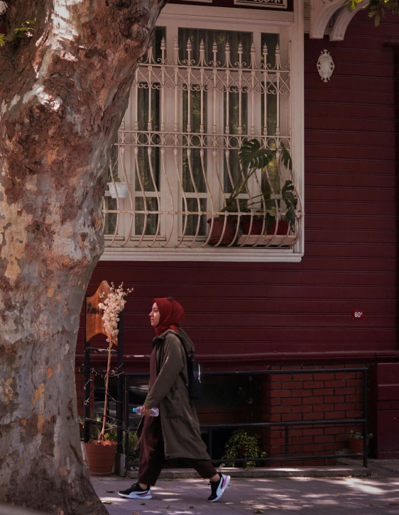 a woman walks in front of a red house on the sidewalk