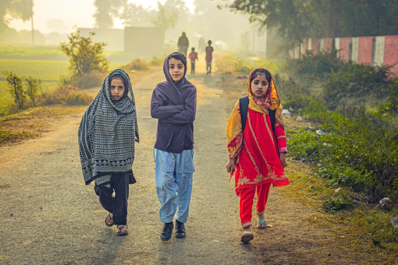 three girls wearing colorful sari are on a dirt road