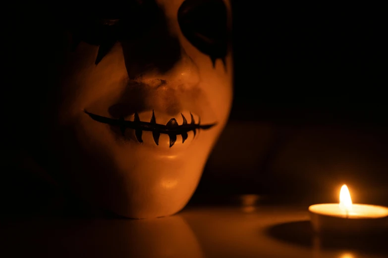 a scary mask with teeth is on a table next to a lit candle
