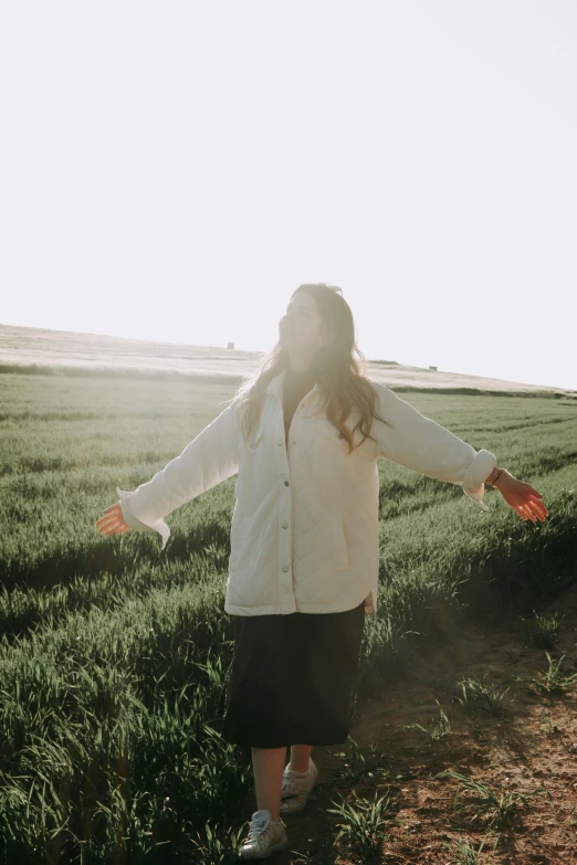 a young woman standing in the grass near a field