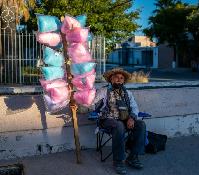 a man sitting on a chair wearing a straw hat and holding a pink item