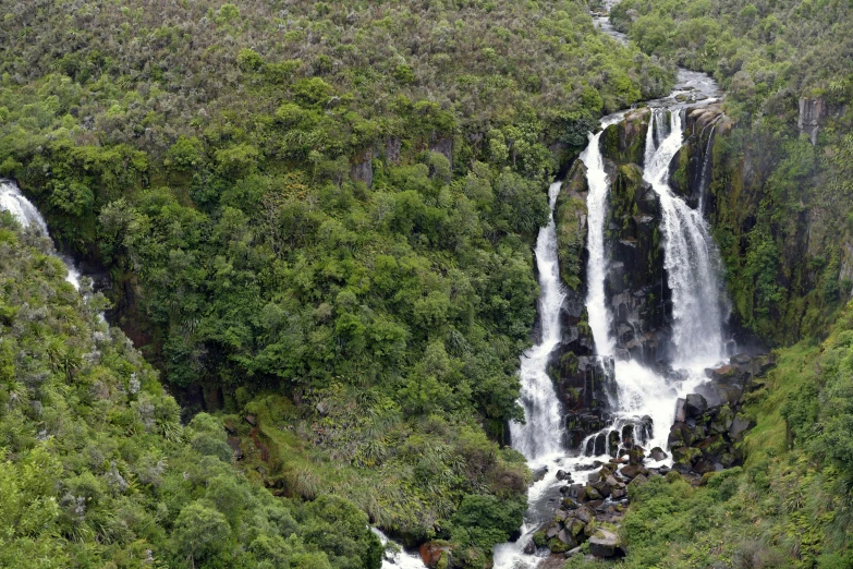 a large waterfall near the mountains surrounded by trees