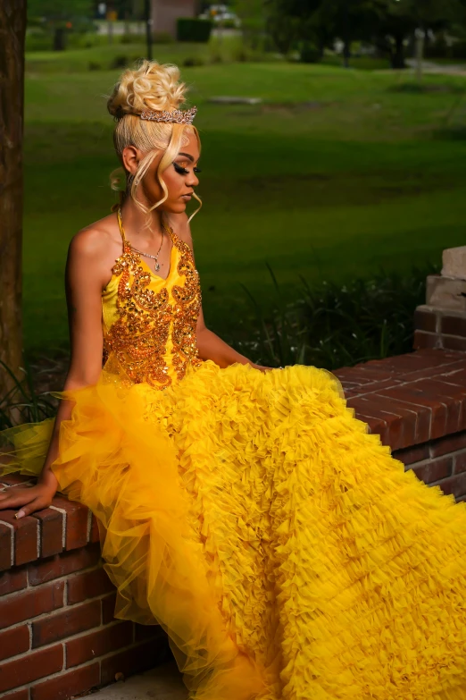 a woman in yellow dresses sitting against a brick wall