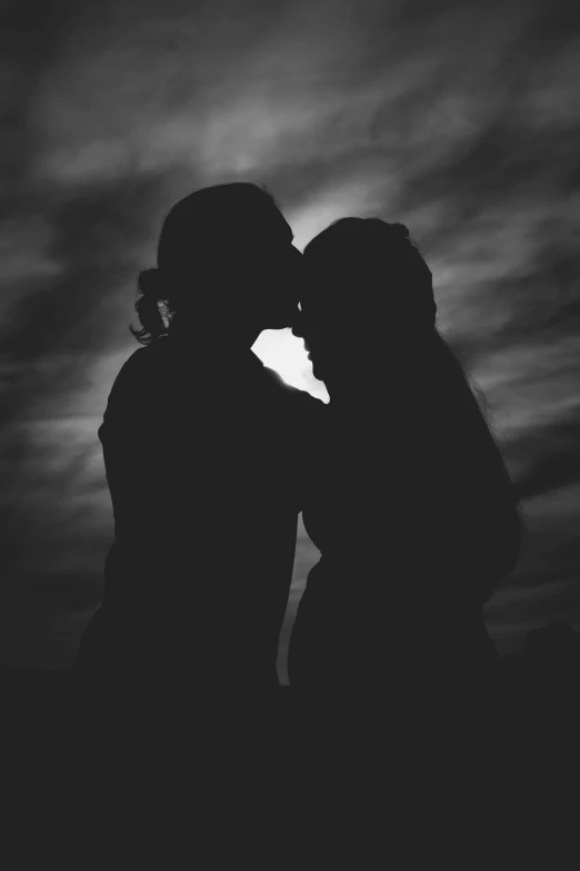 the silhouette of two girls kissing against a dark background