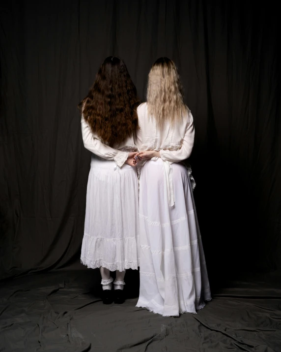 two women are dressed in white, holding hands behind their backs