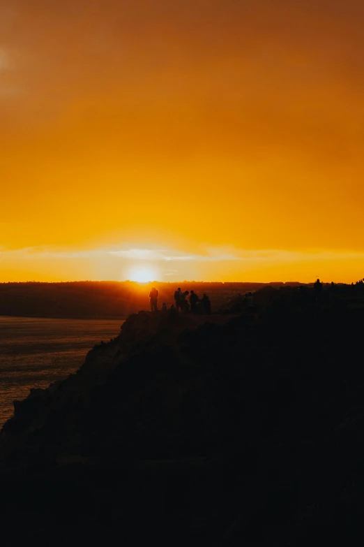 a silhouette of people with surfboards in the sun setting