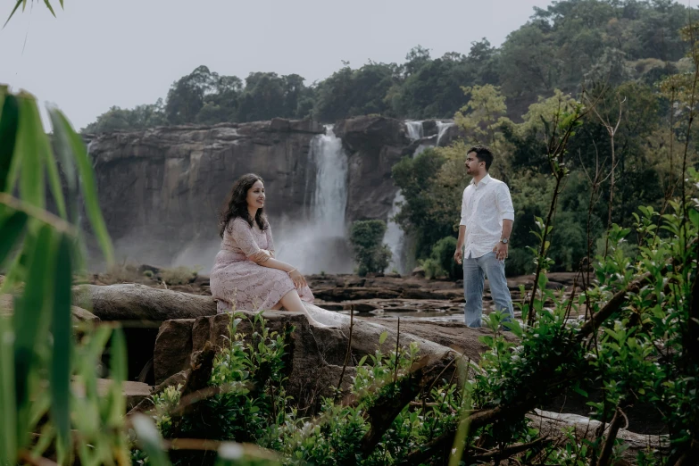 a woman and a man standing on rocks in front of a waterfall