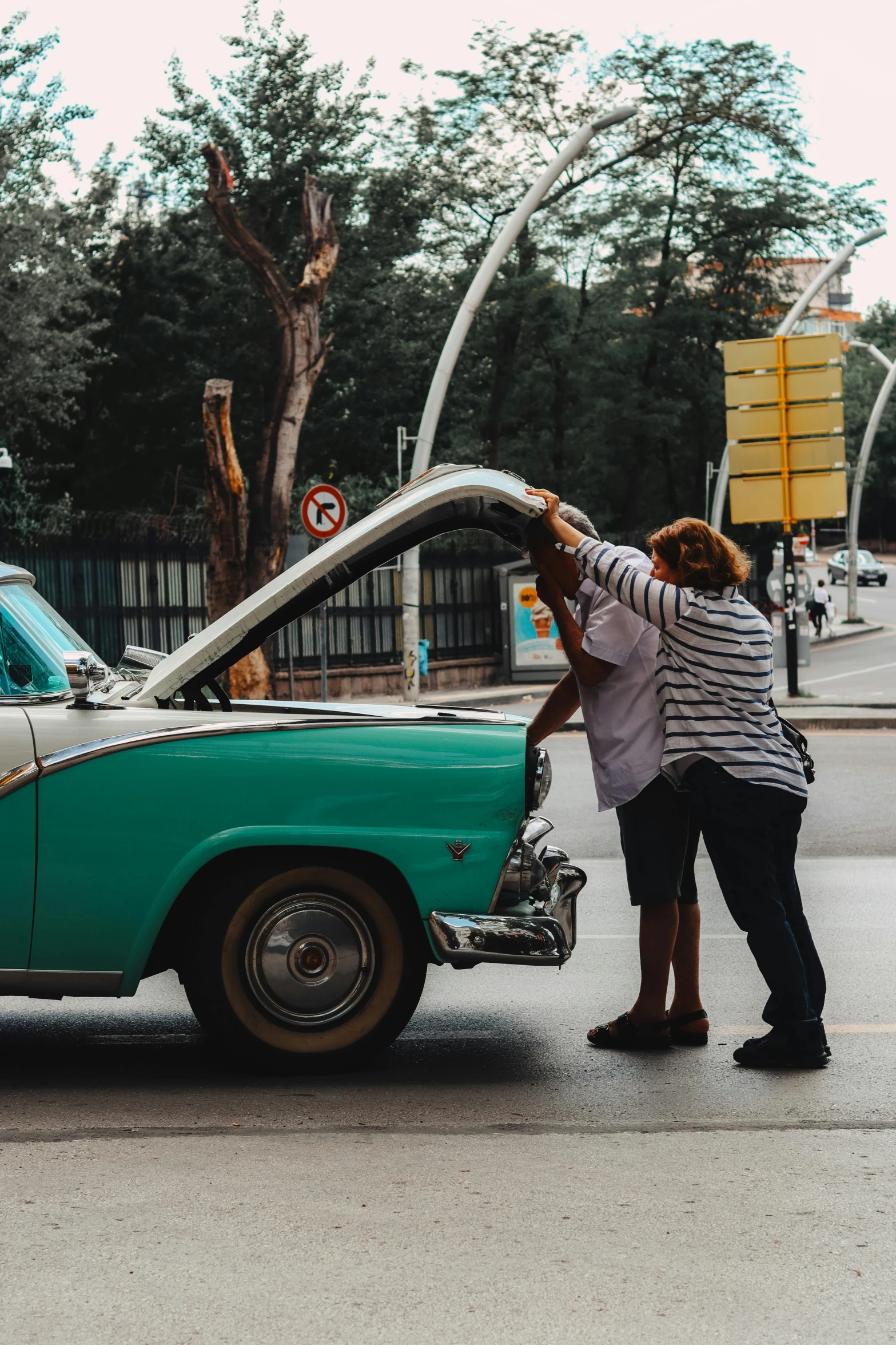 two people hing up the front windshield of an old car