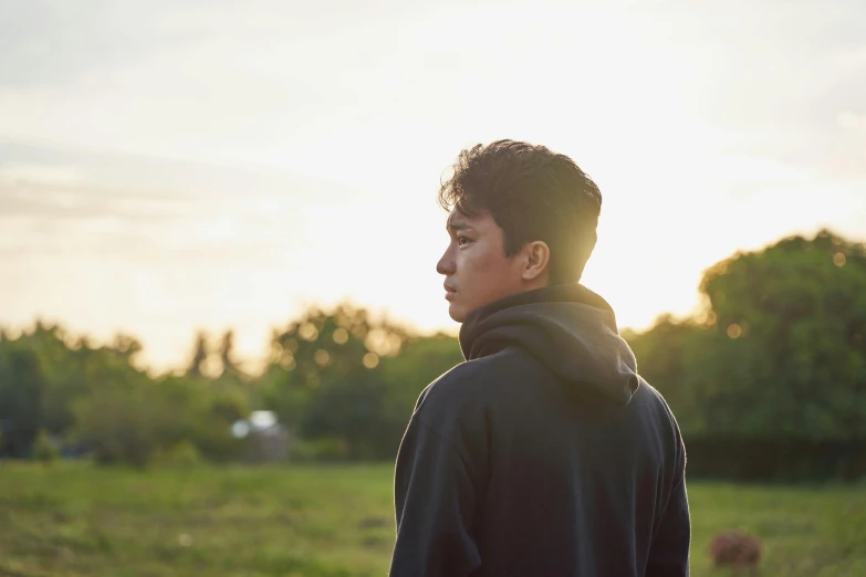 a young man in a hoodie walking through a grass field