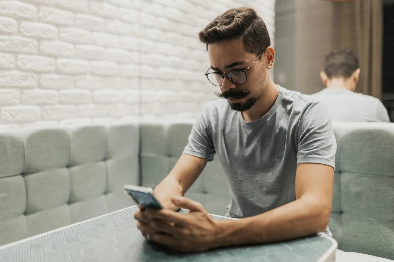 a man with eye glasses and beard looking at his cell phone