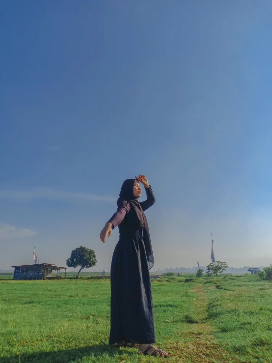 a woman in black dress standing in a field of grass and holding up a cellphone