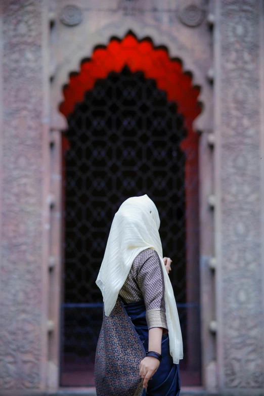 a woman in a headscarf is walking by an ornate building