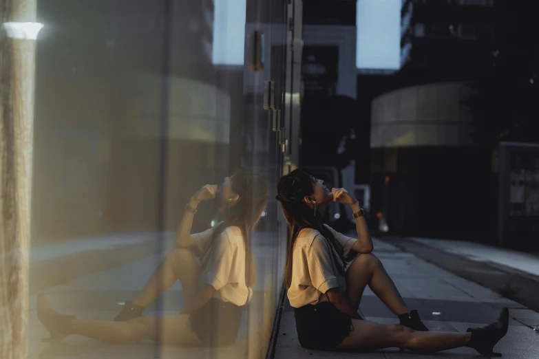 woman sitting on sidewalk smoking a cigarette looking at window