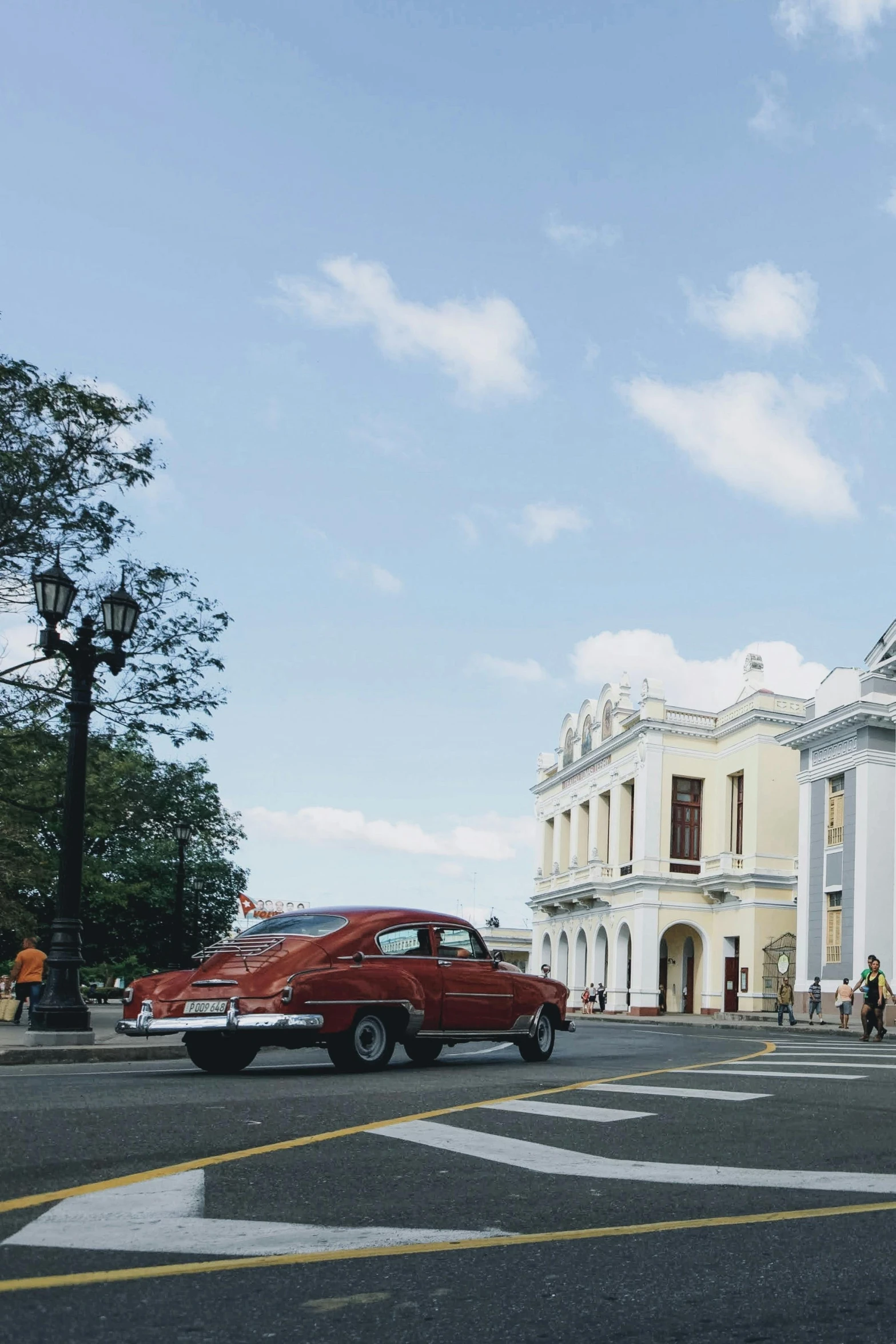 old fashioned red car sits in front of an antique white building