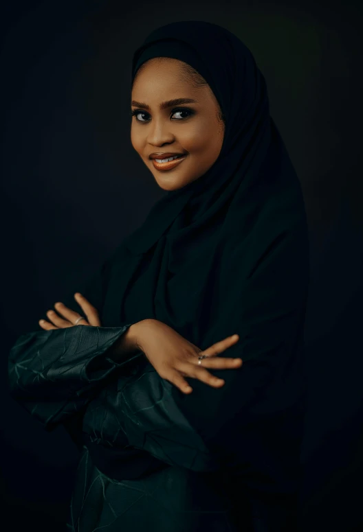 a woman wearing a black hijab stands with her arms folded