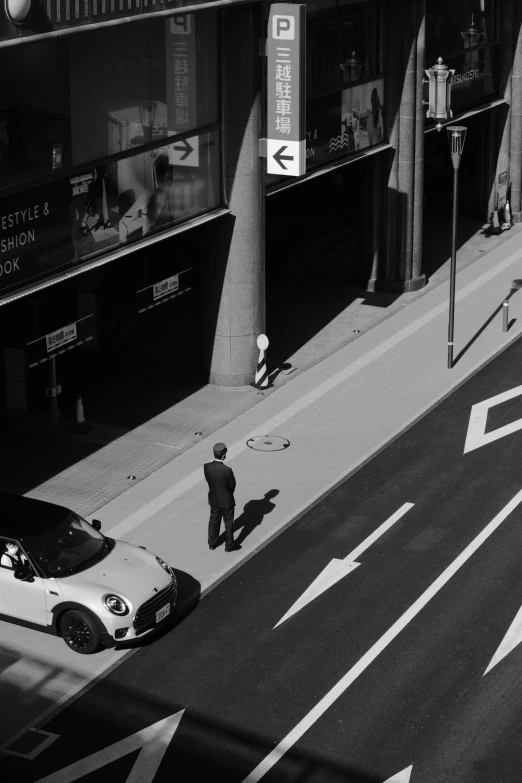 black and white pograph of a person walking on street with parked car