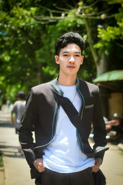 a young man standing on a sidewalk holding his tie in one hand and his head turned sideways