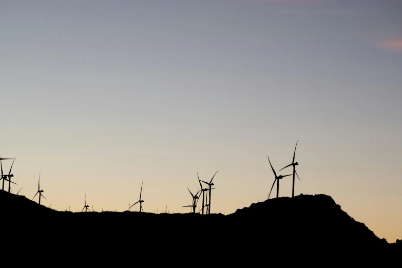 several windmills sit on top of the hill at sunset