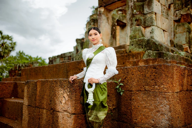 a woman standing next to the wall in front of trees