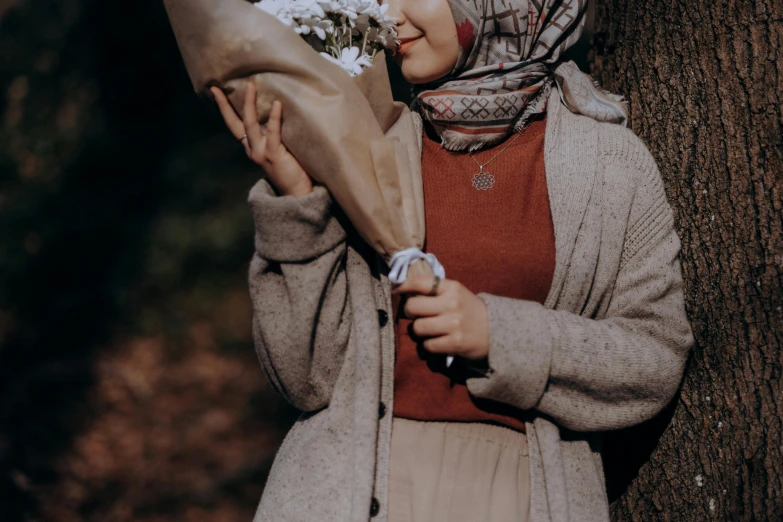 a young lady holding a bouquet of flowers near a tree