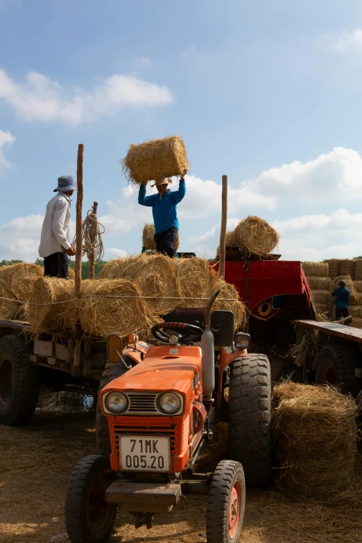 some men loading a load of hay on top of a tractor