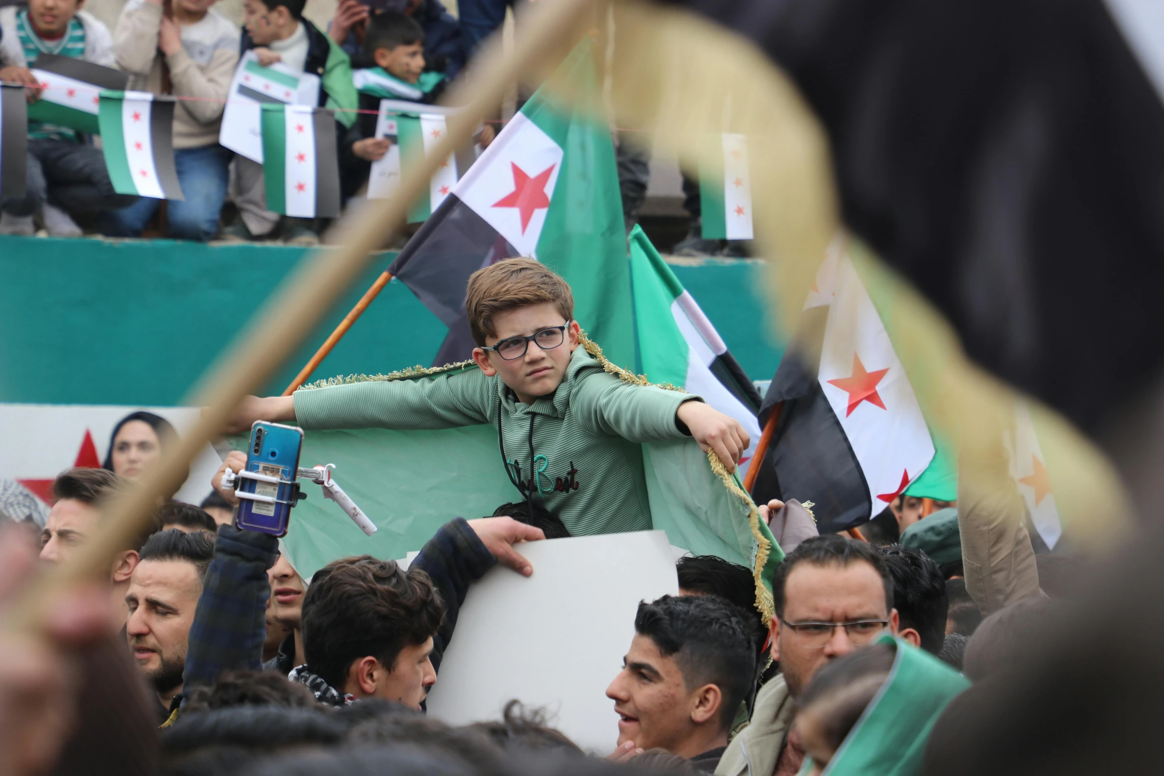 a man taking a picture on his cell phone as he holds the flag of jordan