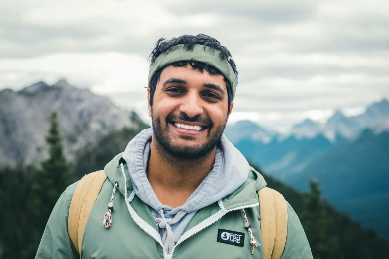 a man smiles into the camera in a mountainous area