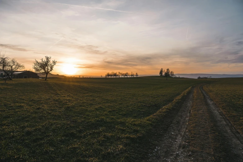 the sun setting on the horizon over a dirt road