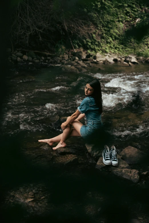 a girl sitting on rocks near a stream