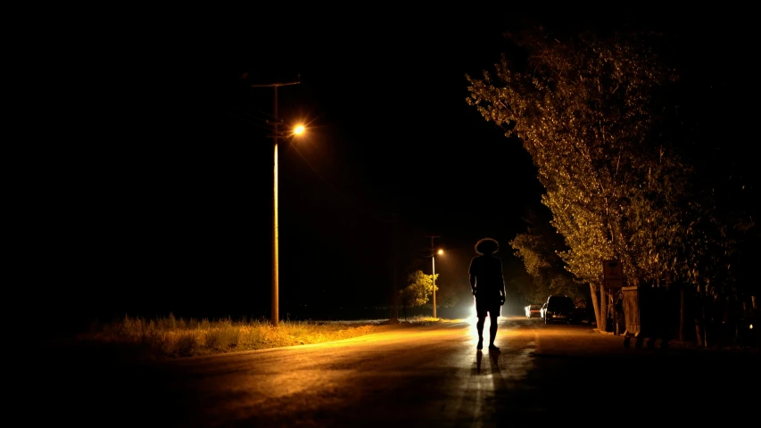 person walking along a dark road with a street lamp